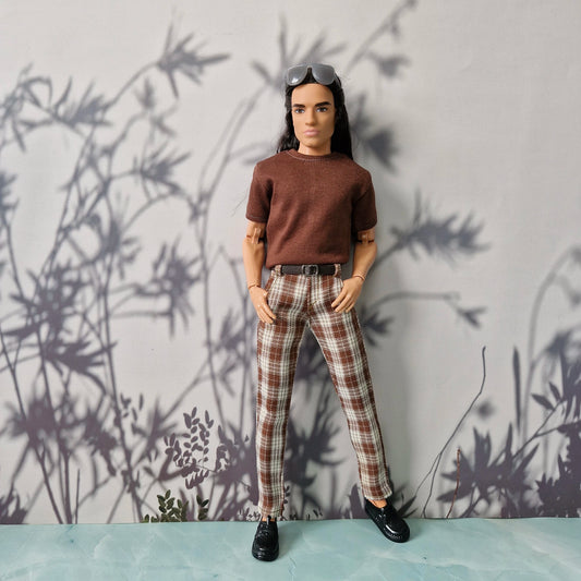Ken Dol wearing a brown shirt and plaid pants against a wall with plant shadows.