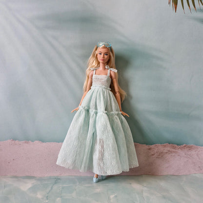 Blonde Barbie doll in pastel mint lace gown standing on beach inspired background