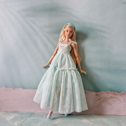 Brunette Barbie doll wearing flowing mint lace gown on soft pastel background