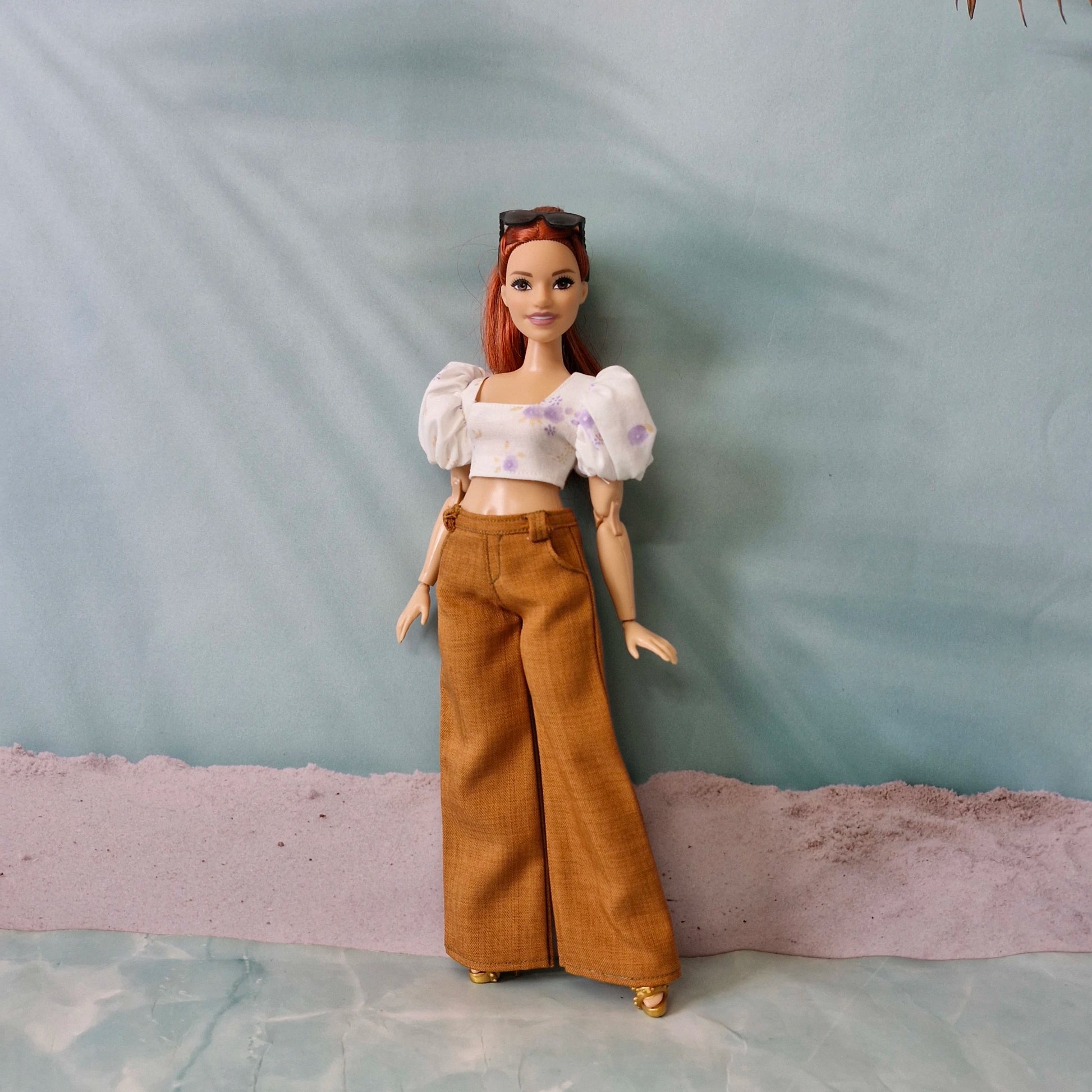 Full body shot of a redhead Curvy Barbie modeling trendy brown wide leg trousers and a floral summer top.
