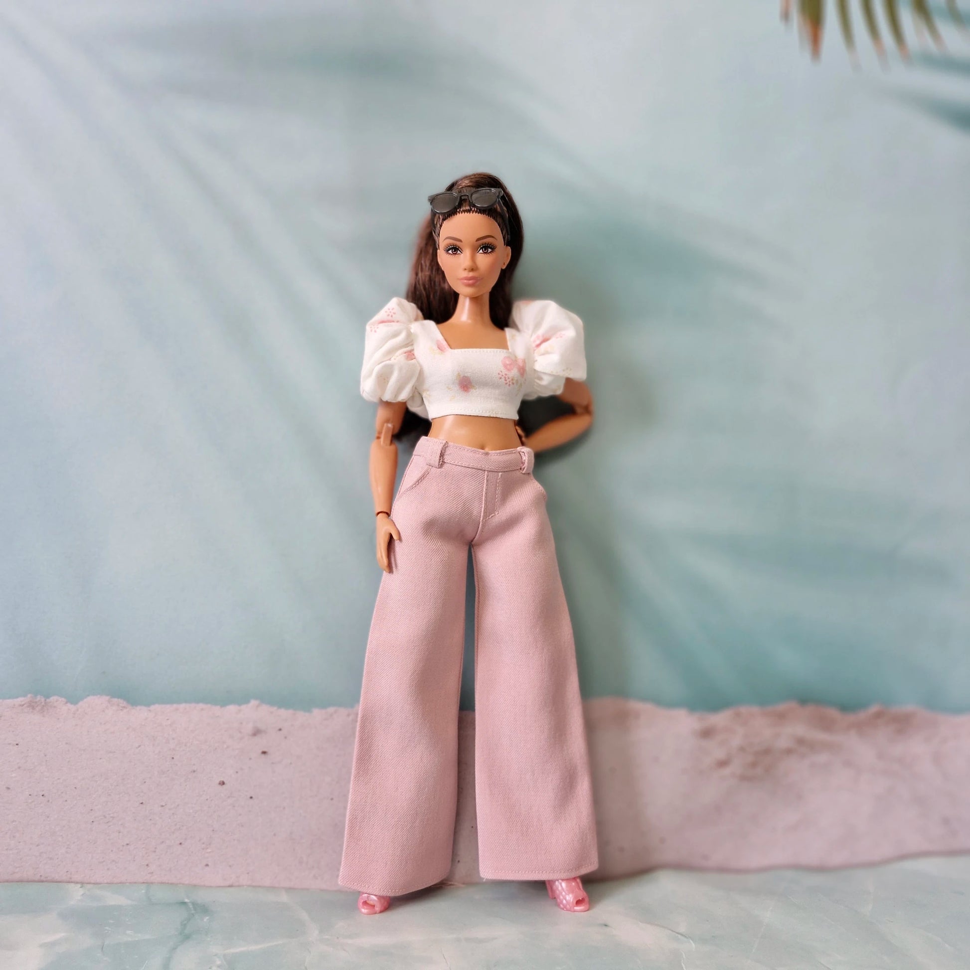 Curvy Barbie doll dressed in chic pink wide leg pants and a matching white crop top with pink floral patterns.