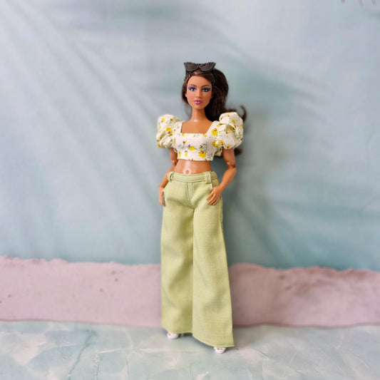 Brunette Curvy Barbie doll wearing light green wide leg pants and a white crop top with yellow floral print.