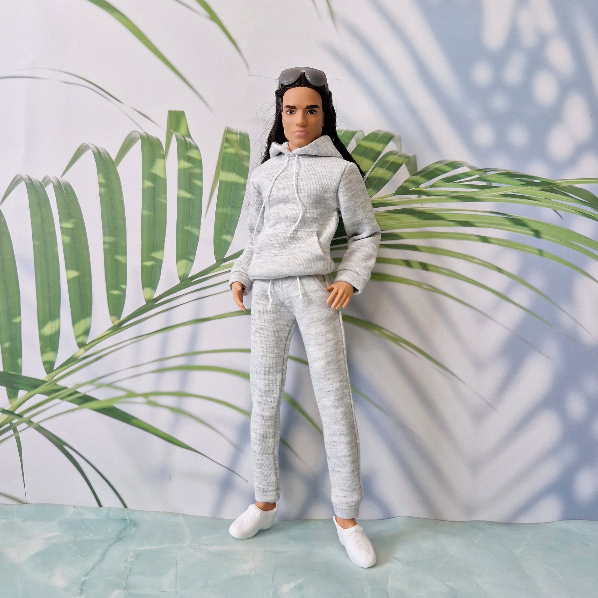 Long-haired Ken doll modeling a realistic grey heathered tracksuit with white drawstrings and white sneakers.