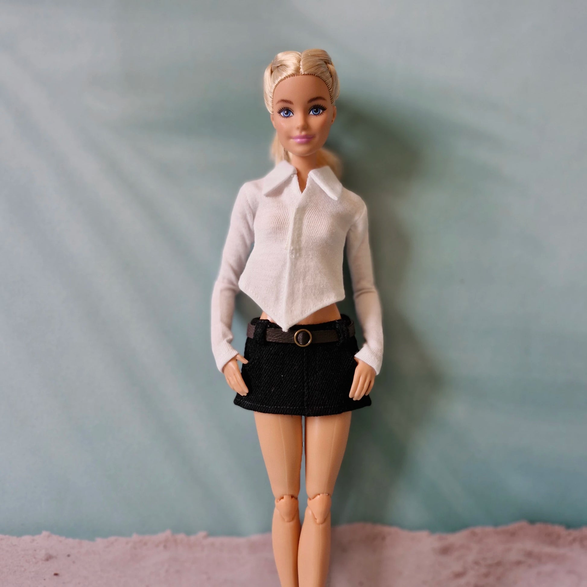Barbie doll showcasing a classic white pointed hem collared shirt and black belted mini skirt.