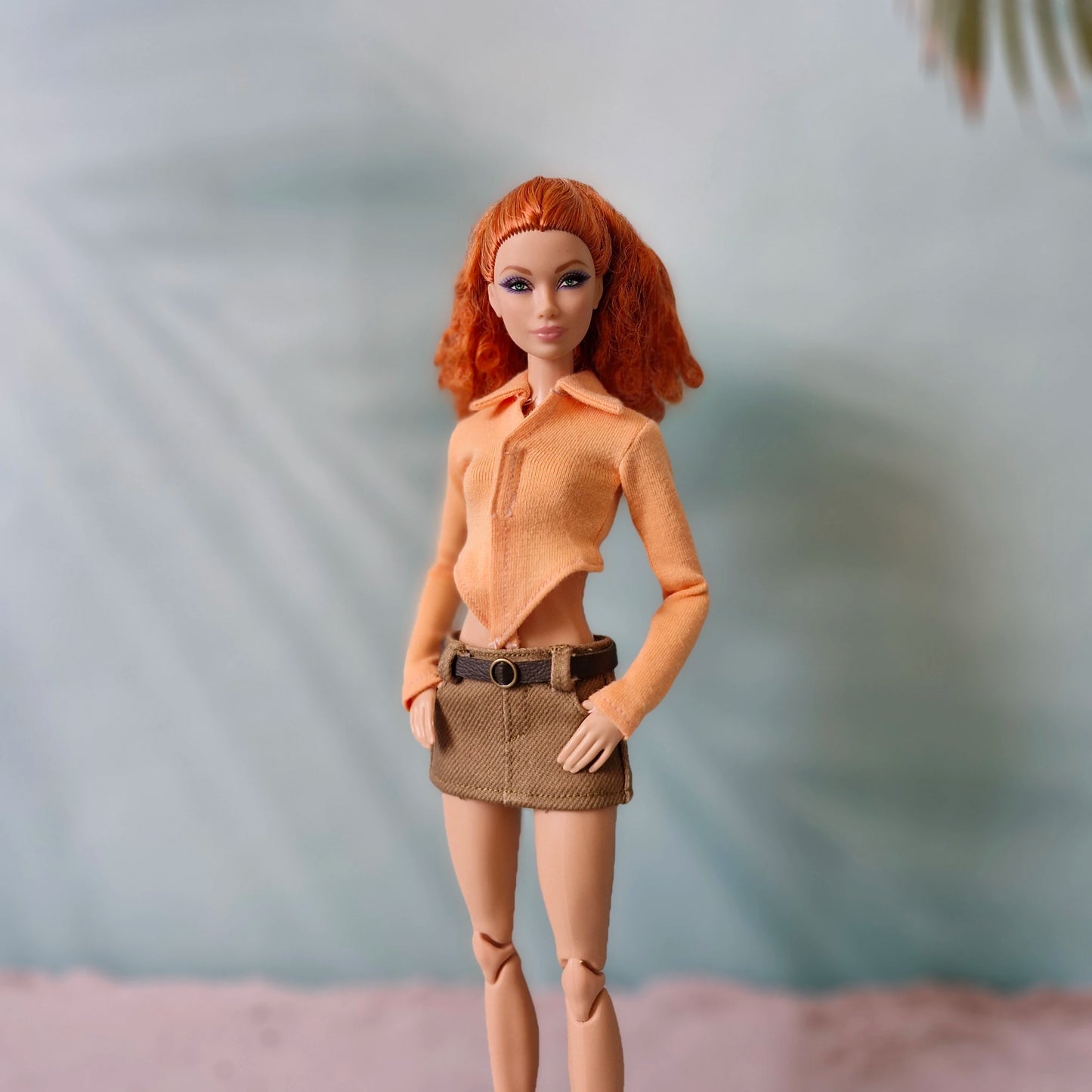 Red-haired Barbie doll wearing a peach orange pointed hem top and brown mini skirt.