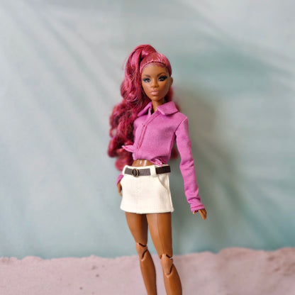 Barbie doll with pink hair wearing a magenta pointed hem shirt and white mini skirt.