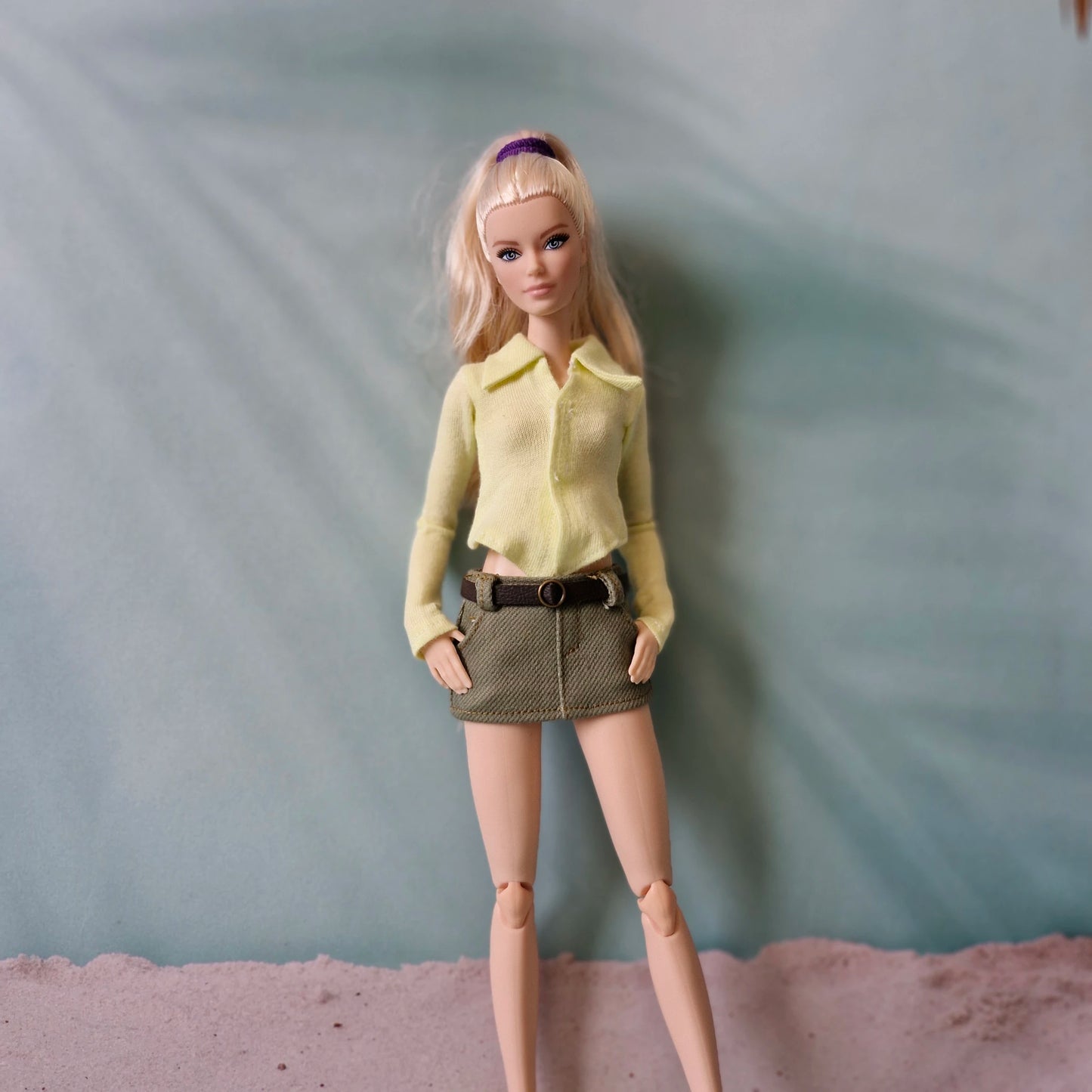 Barbie doll wearing a yellow shirt and brown skirt against a plain background