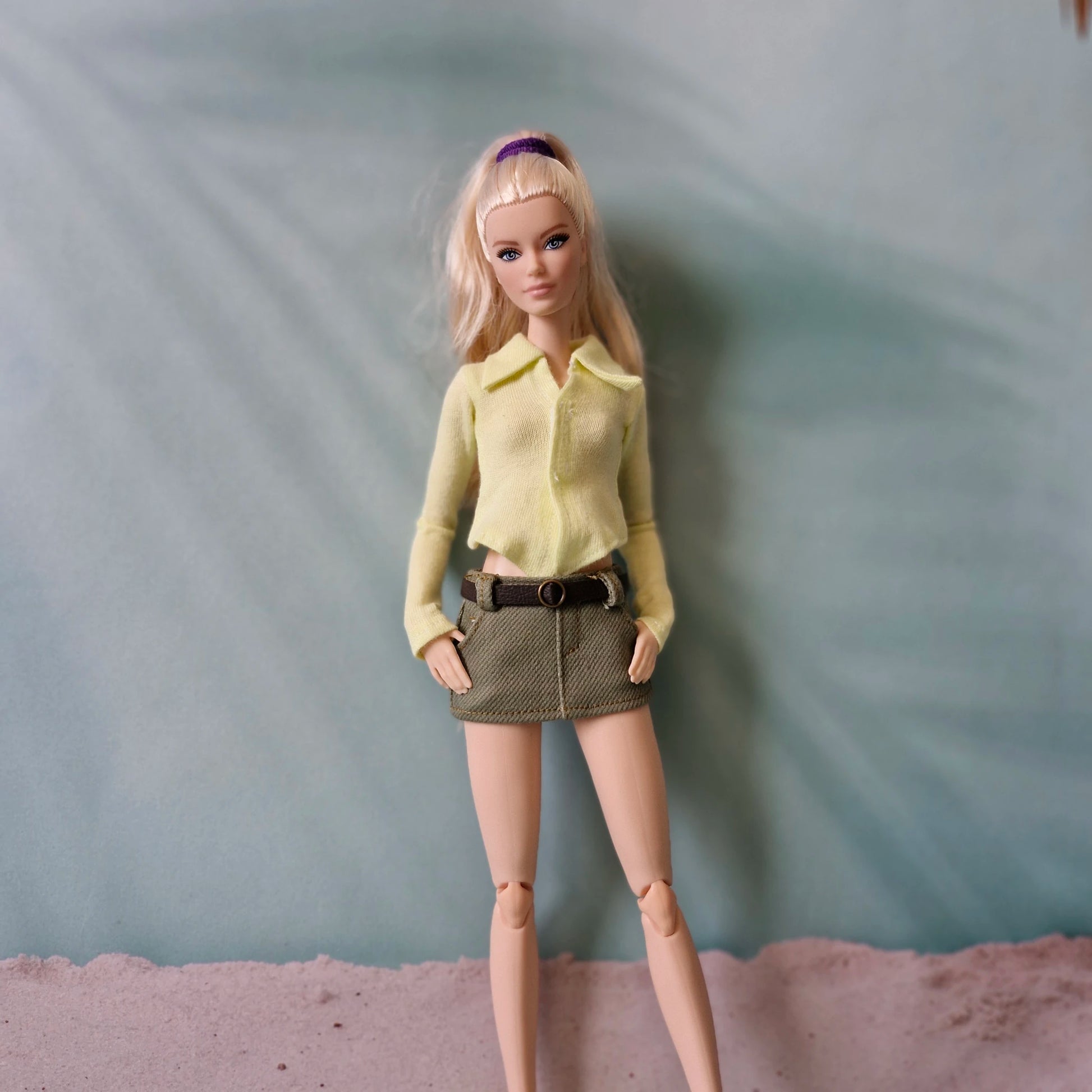 Barbie doll wearing a yellow shirt and brown skirt against a plain background