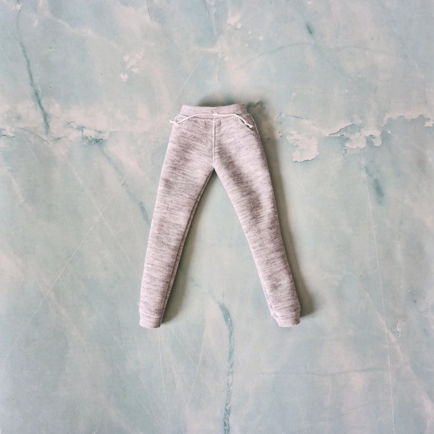 Flat lay of grey heathered doll sweatpants with an elastic waistband, white drawstrings, and cuffed ankles.