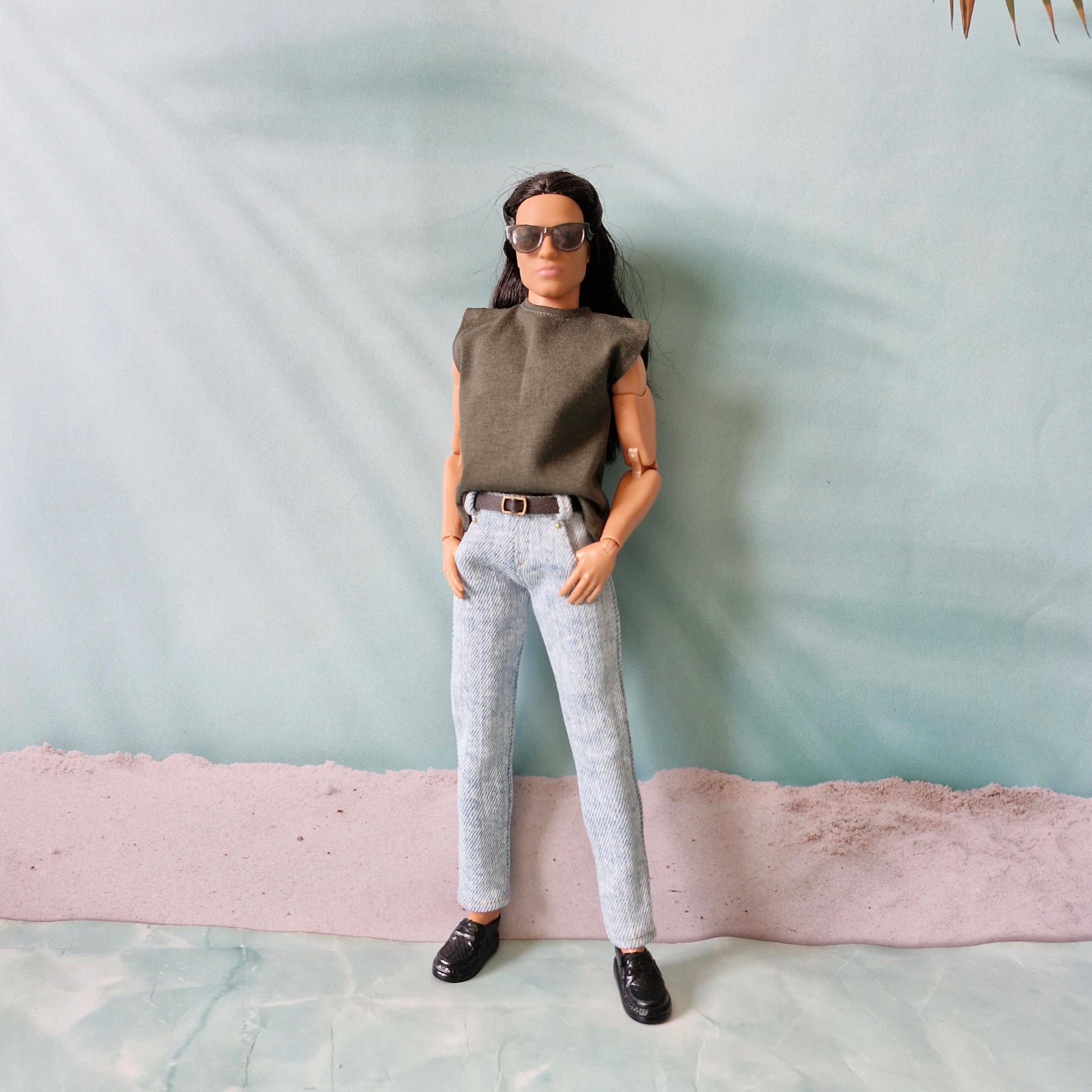 Ken doll wearing an olive green sleeveless t-shirt tucked into light blue washed denim jeans.
