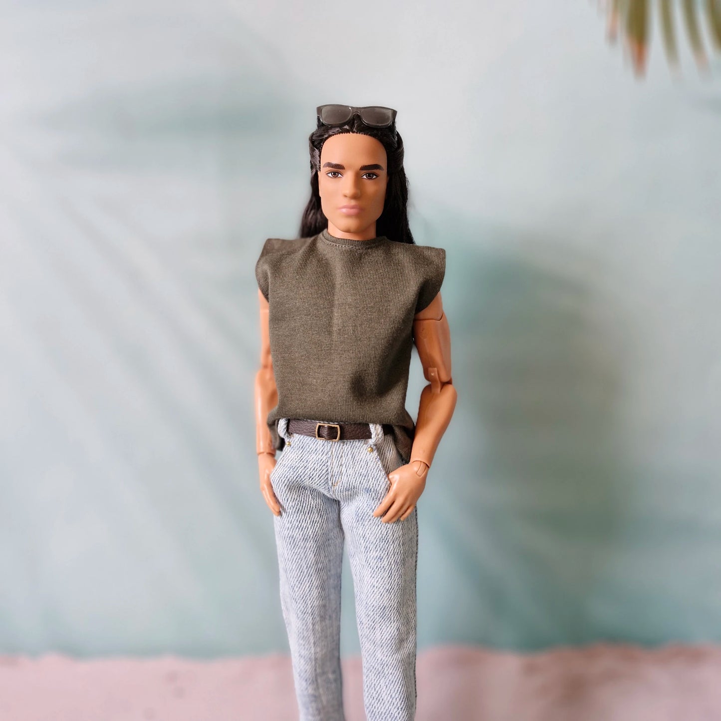 Close-up of a Ken doll wearing a casual olive green muscle tee and light wash jeans with a brown belt.