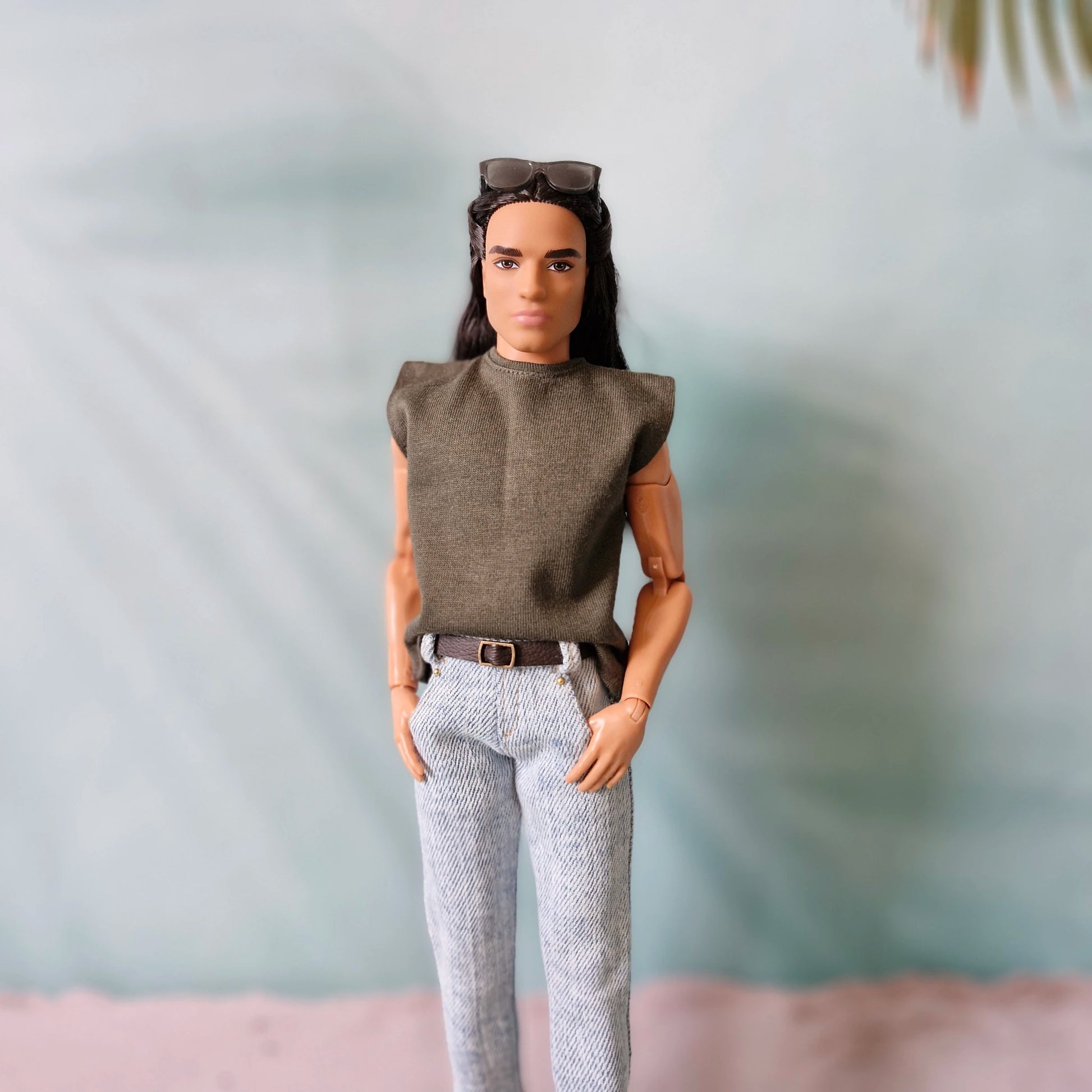 Close-up of a Ken doll wearing a casual olive green muscle tee and light wash jeans with a brown belt.