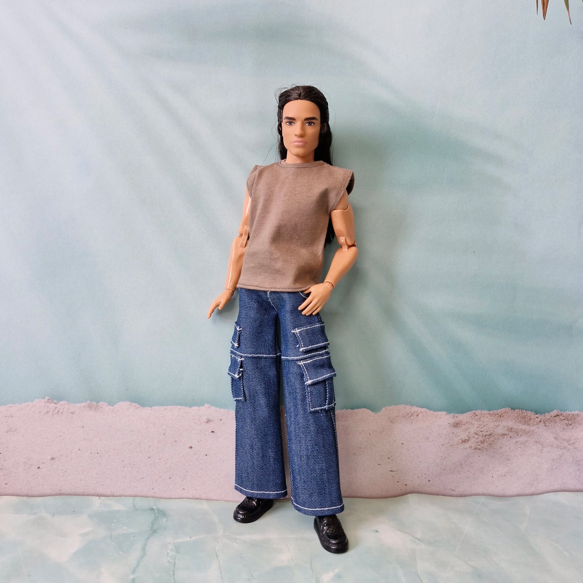 Full body shot of a Ken doll wearing a casual brown sleeveless shirt and trendy dark denim cargo pants with pockets.