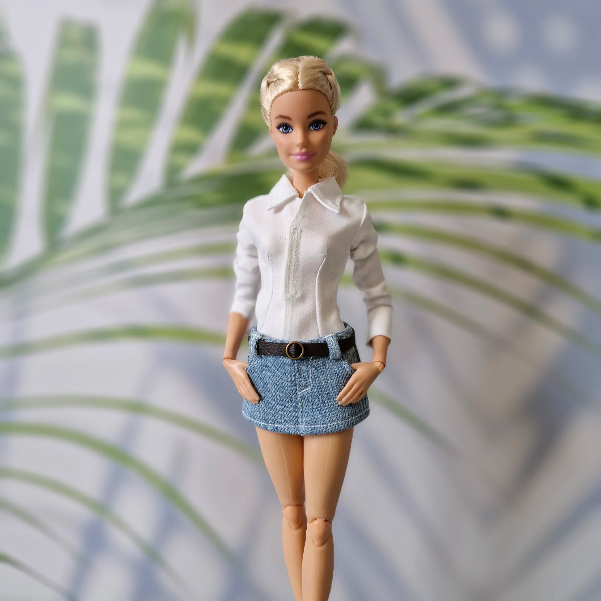 Close-up of Barbie doll modeling a classic white button-down shirt and a belted light wash denim mini skirt.