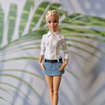 Close-up of Barbie doll modeling a classic white button-down shirt and a belted light wash denim mini skirt.