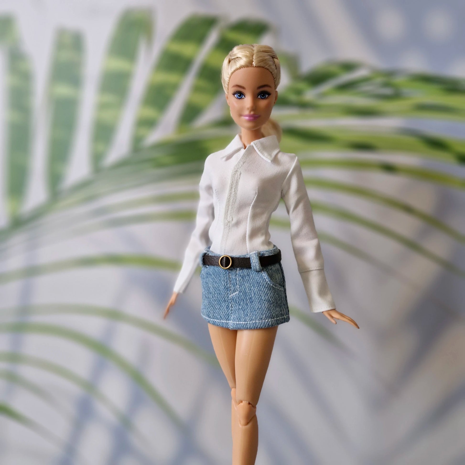 Fashionable Barbie doll dressed in a tailored white long-sleeve shirt and blue jean mini skirt.