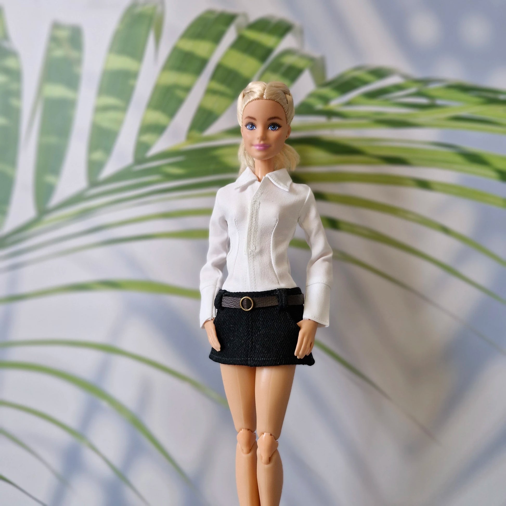Blonde Barbie doll wearing a chic white long-sleeve shirt and a black mini skirt with a brown belt.