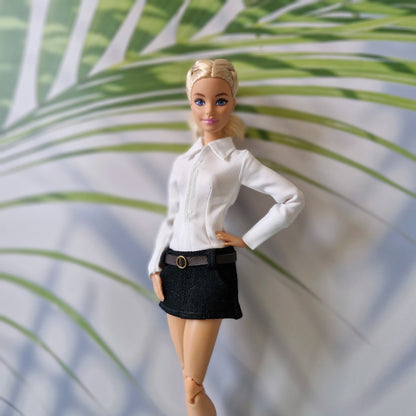Close-up of Barbie doll modeling a classic white collared top and tailored black mini skirt.