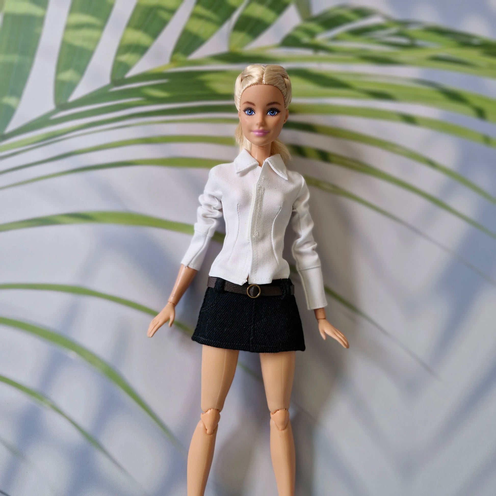 Barbie doll dressed in a smart casual outfit featuring a white long-sleeve shirt and a black mini skirt.
