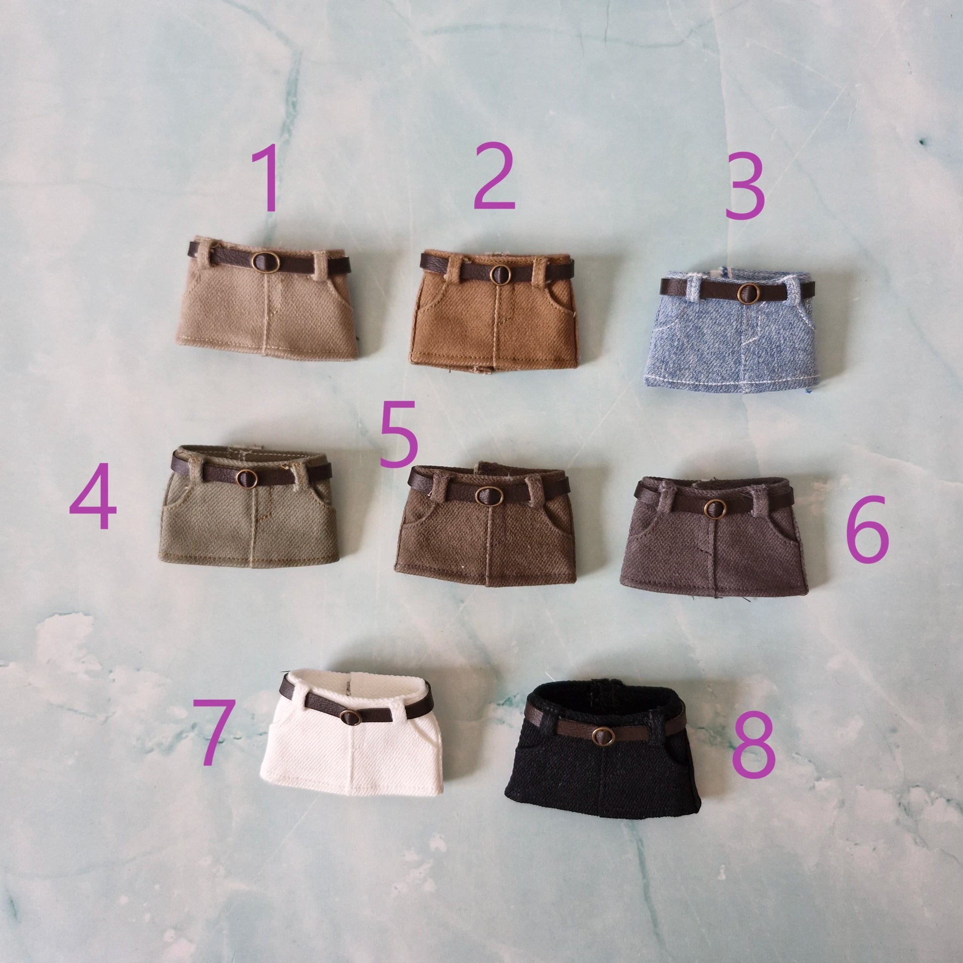 Collection of 8 miniature doll mini skirts with belts, available in beige, camel, blue denim, olive green, dark brown, grey, white, and black.