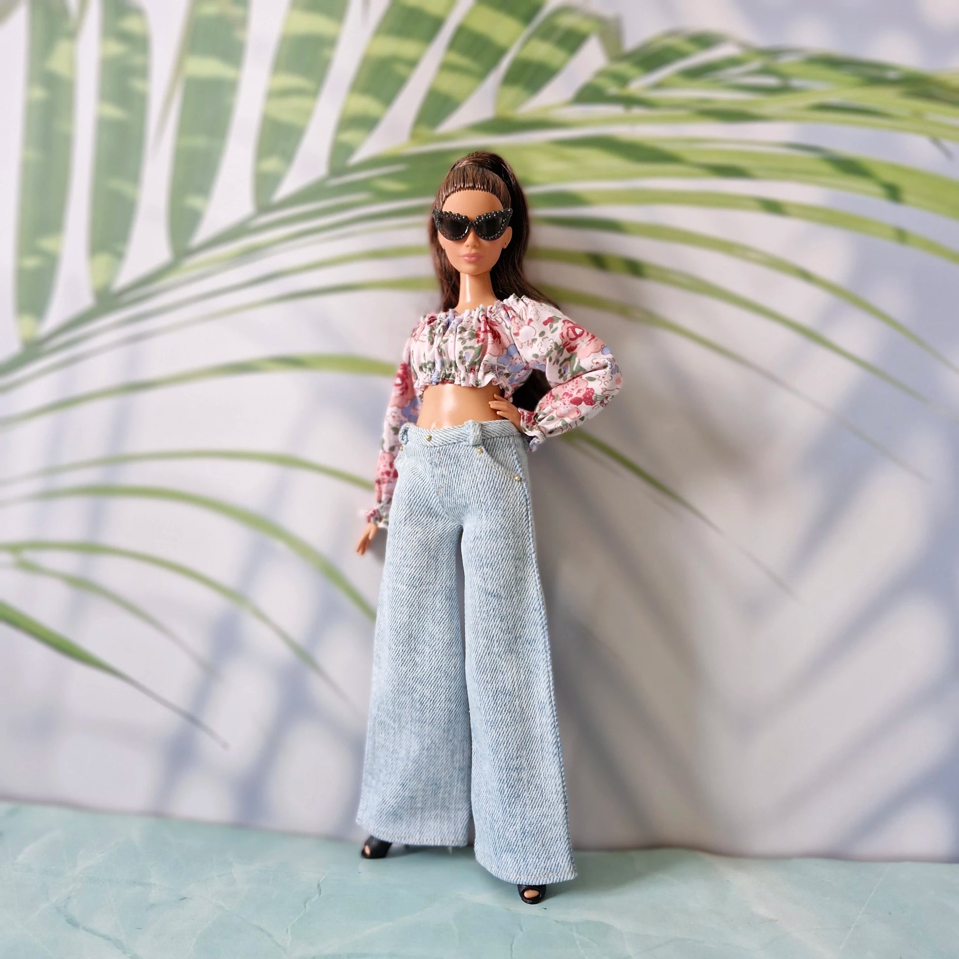 Curvy Barbie wearing a floral off-the-shoulder crop top and light blue wide-leg jeans, posing with black sunglasses.