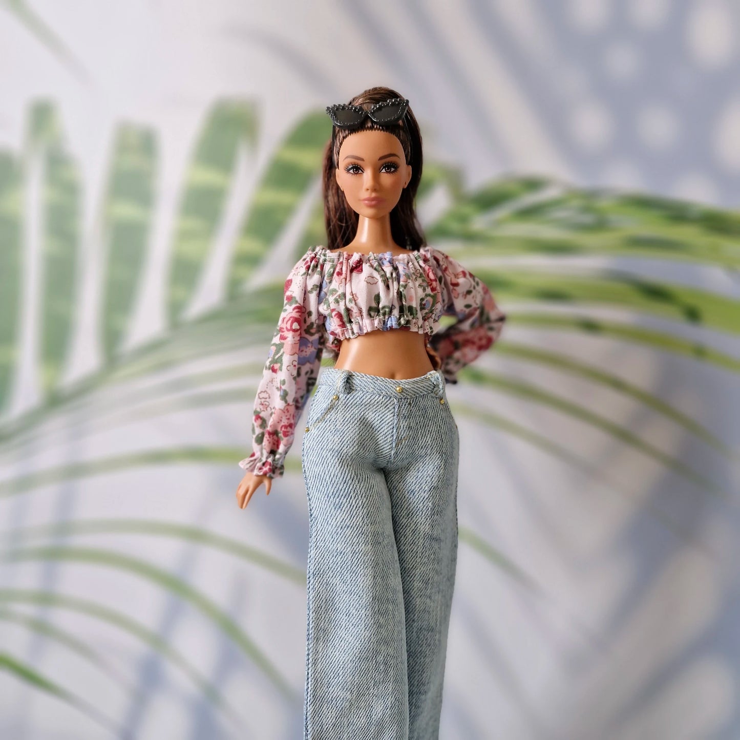 Close up of Curvy Barbie doll modeling a long-sleeved floral crop top and high-waisted light wash denim pants.