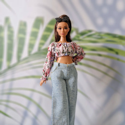 Close up of Curvy Barbie doll modeling a long-sleeved floral crop top and high-waisted light wash denim pants.