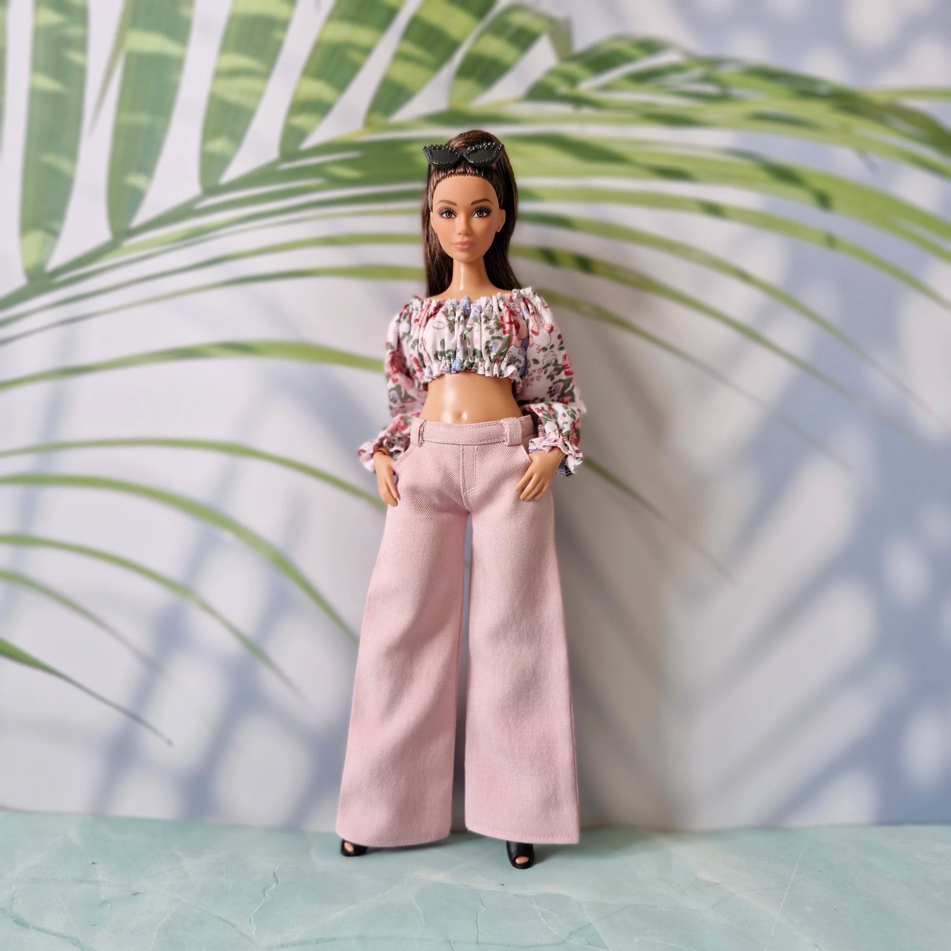 Barbie doll wearing a floral top and pink pants against a leafy background