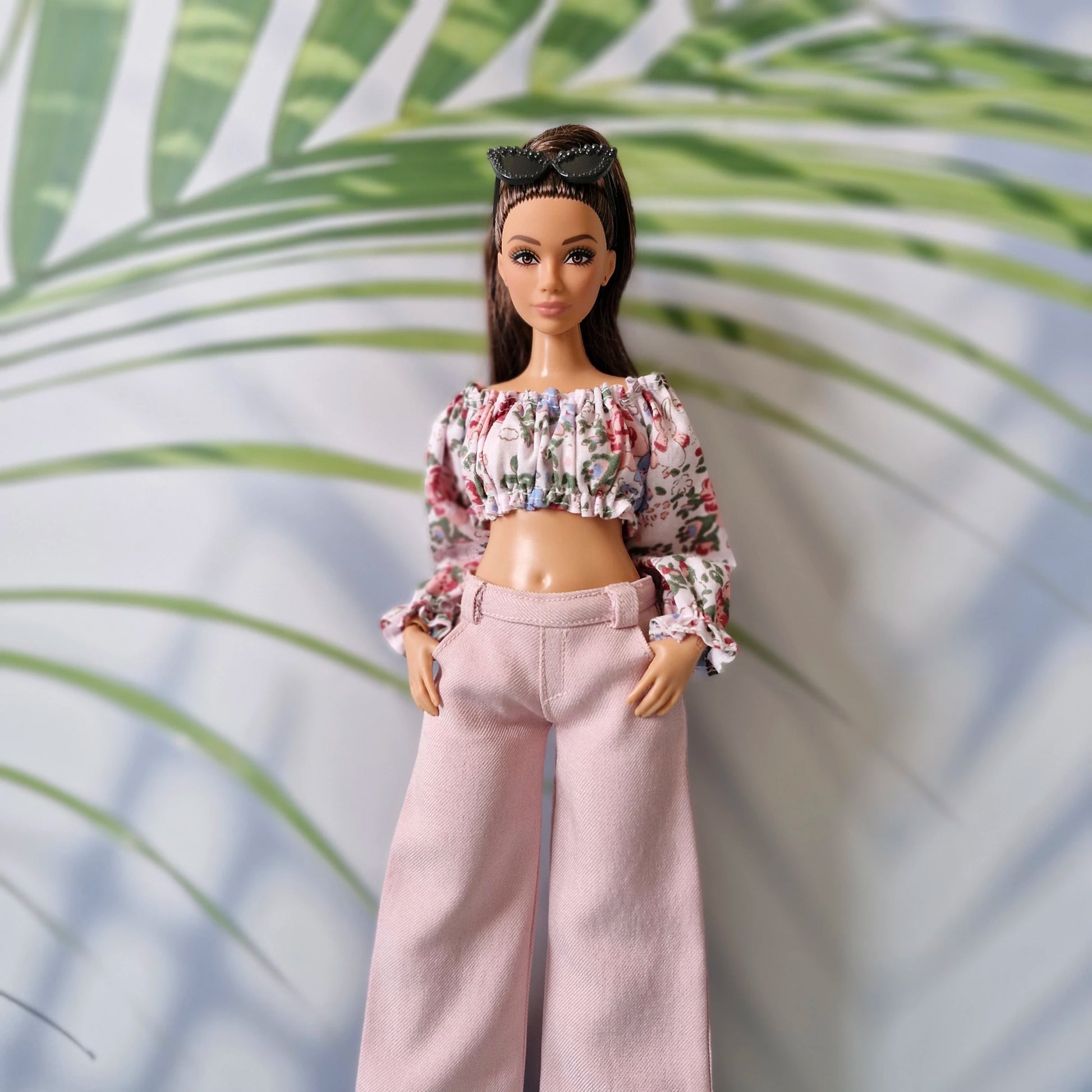 Curvy Barbie dressed in a stylish floral ruffle crop top and pastel pink wide-leg trousers, wearing sunglasses on her head.