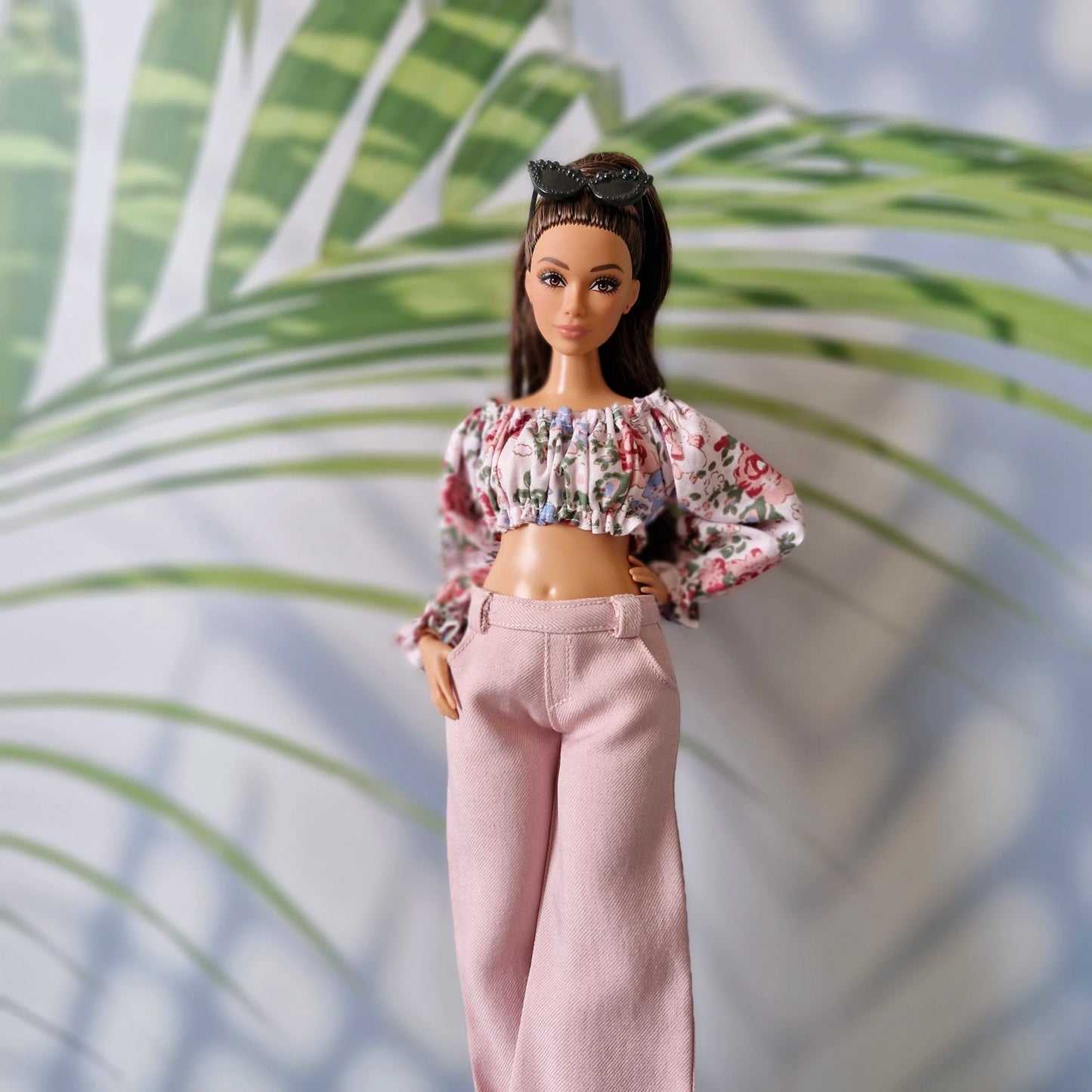Curvy Barbie doll posing in a trendy summer outfit featuring a floral top and light pink high-waisted pants.