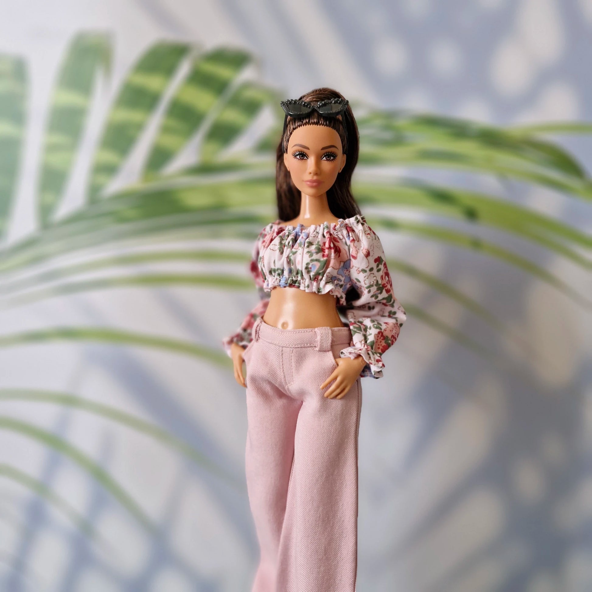 Portrait of a Curvy Barbie looking fashionable in an off-shoulder floral shirt and soft pink wide-leg pants.