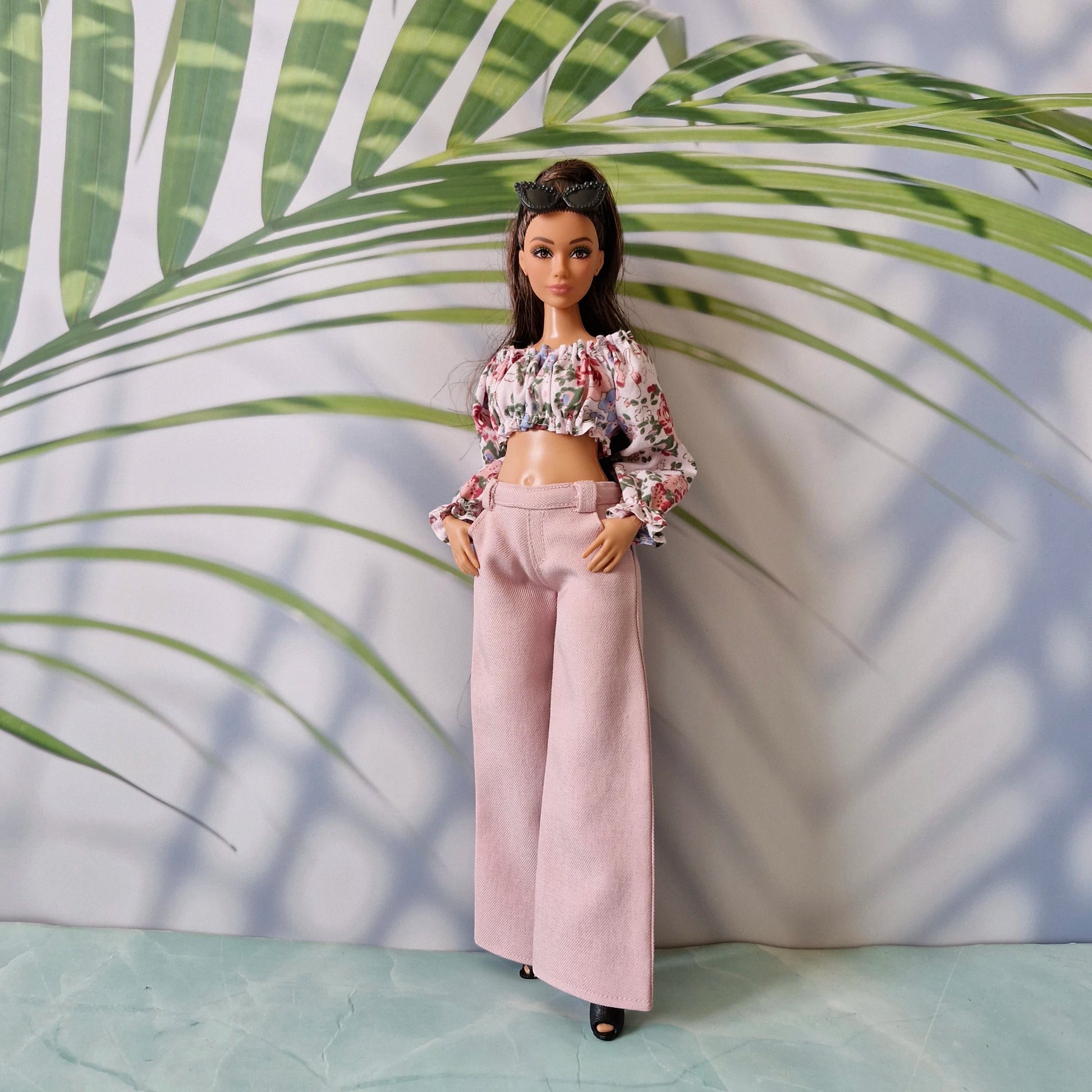Full body shot of a Curvy Barbie doll showcasing a floral long-sleeve crop top paired with pastel pink wide-leg pants.