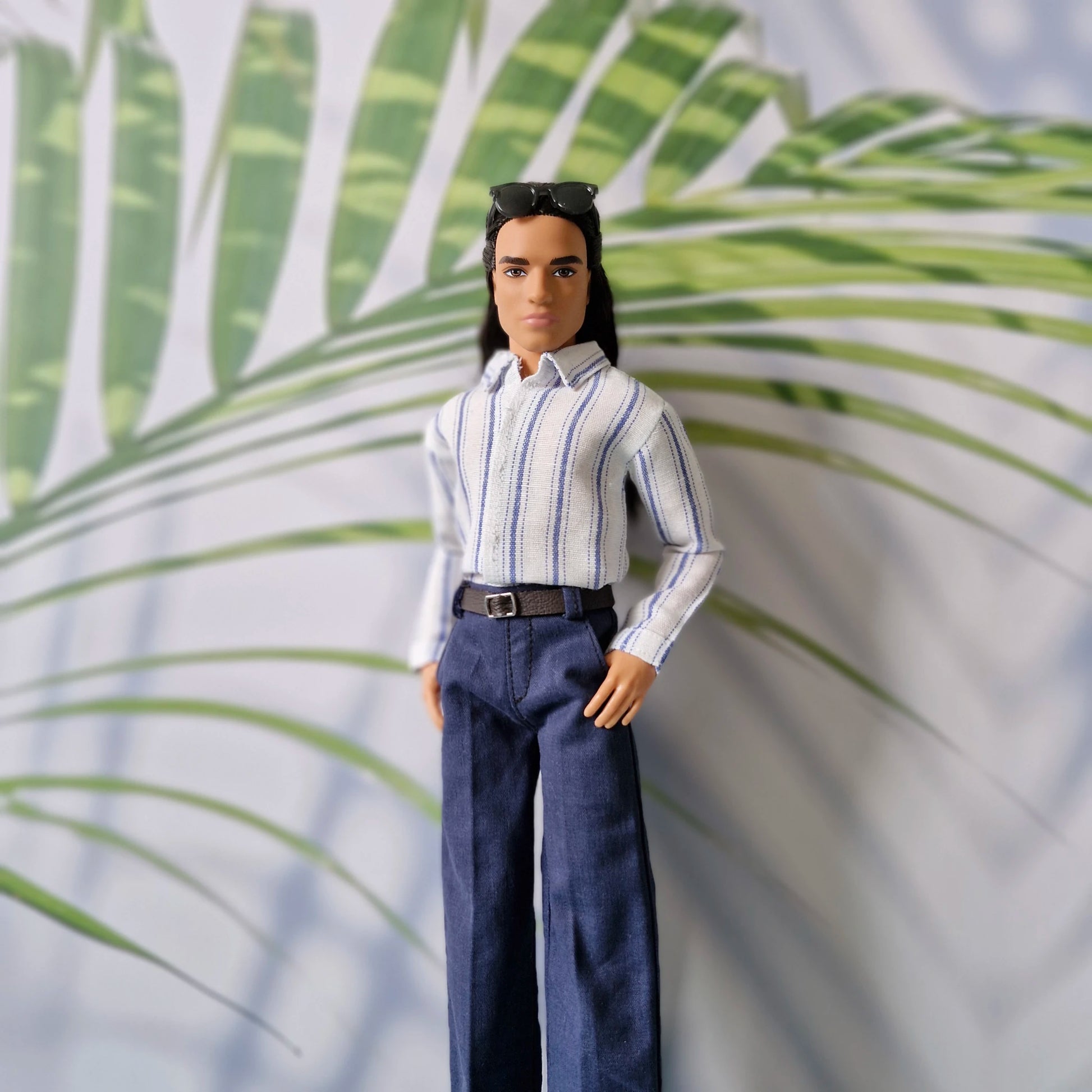 Portrait of a Ken doll looking sharp in a classic blue and white striped collared shirt and dark trousers.