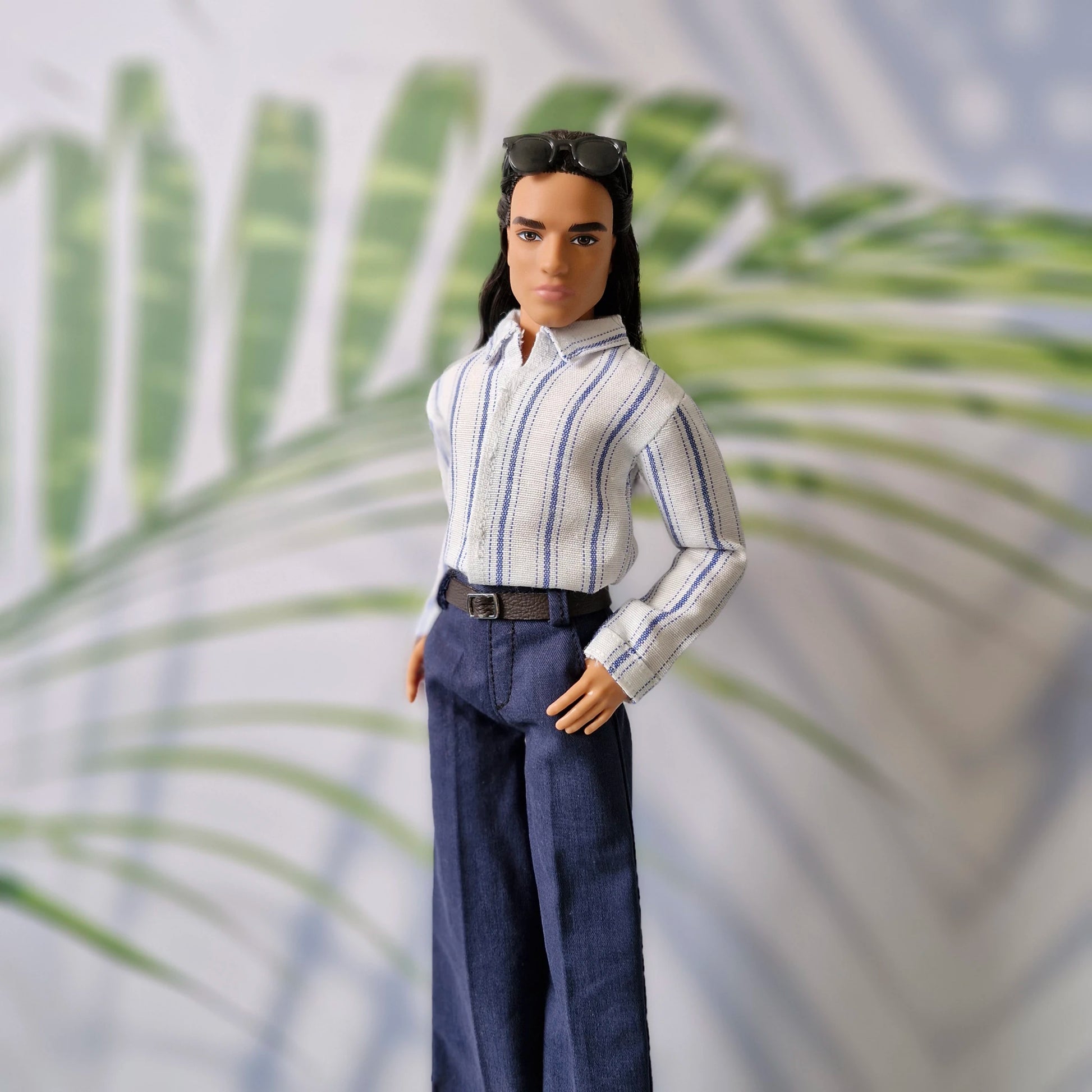 Close-up of a Ken doll modeling a miniature white shirt with blue vertical stripes and navy blue pants with a belt.