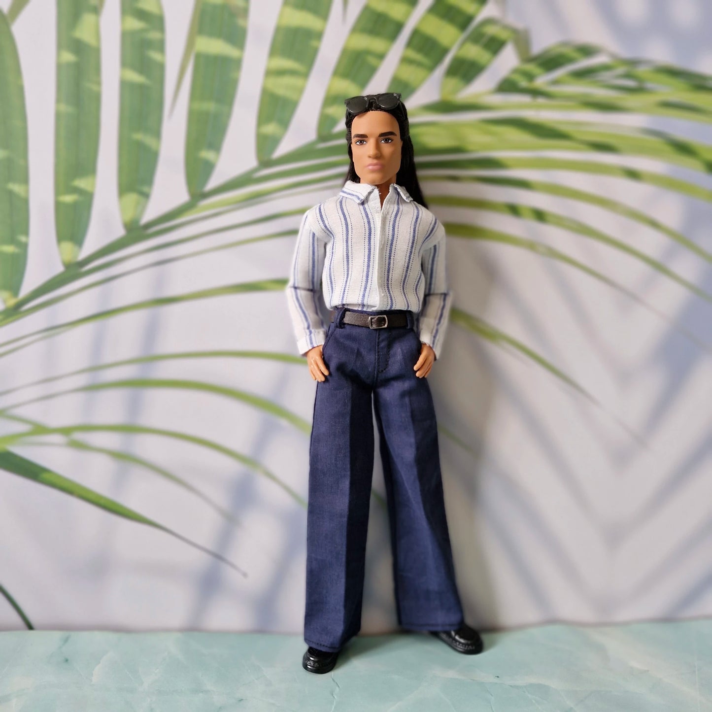 Ken doll fashion featuring a smart-casual look with a tucked-in striped shirt and navy trousers, standing with hands in pockets.
