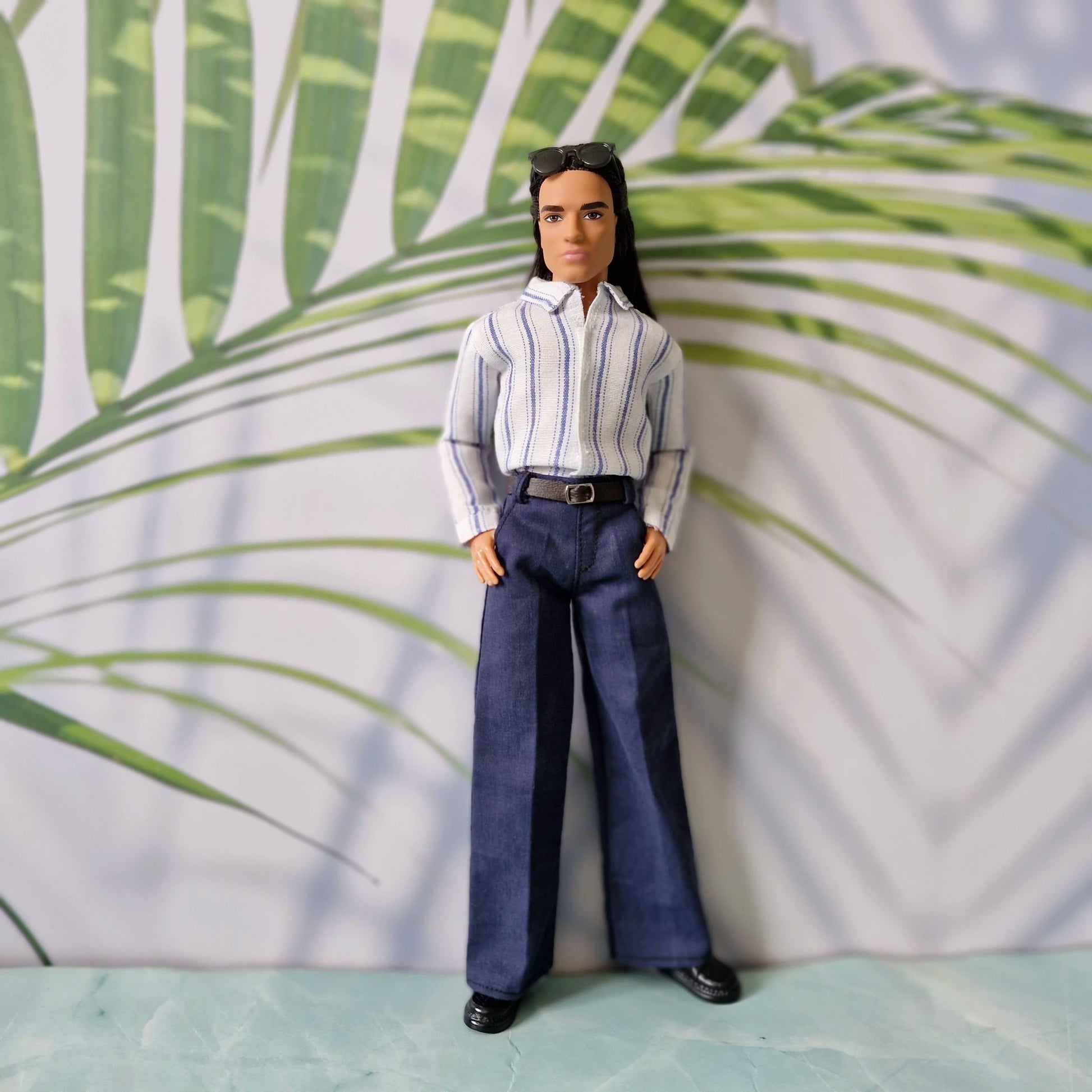 Ken doll fashion featuring a smart-casual look with a tucked-in striped shirt and navy trousers, standing with hands in pockets.