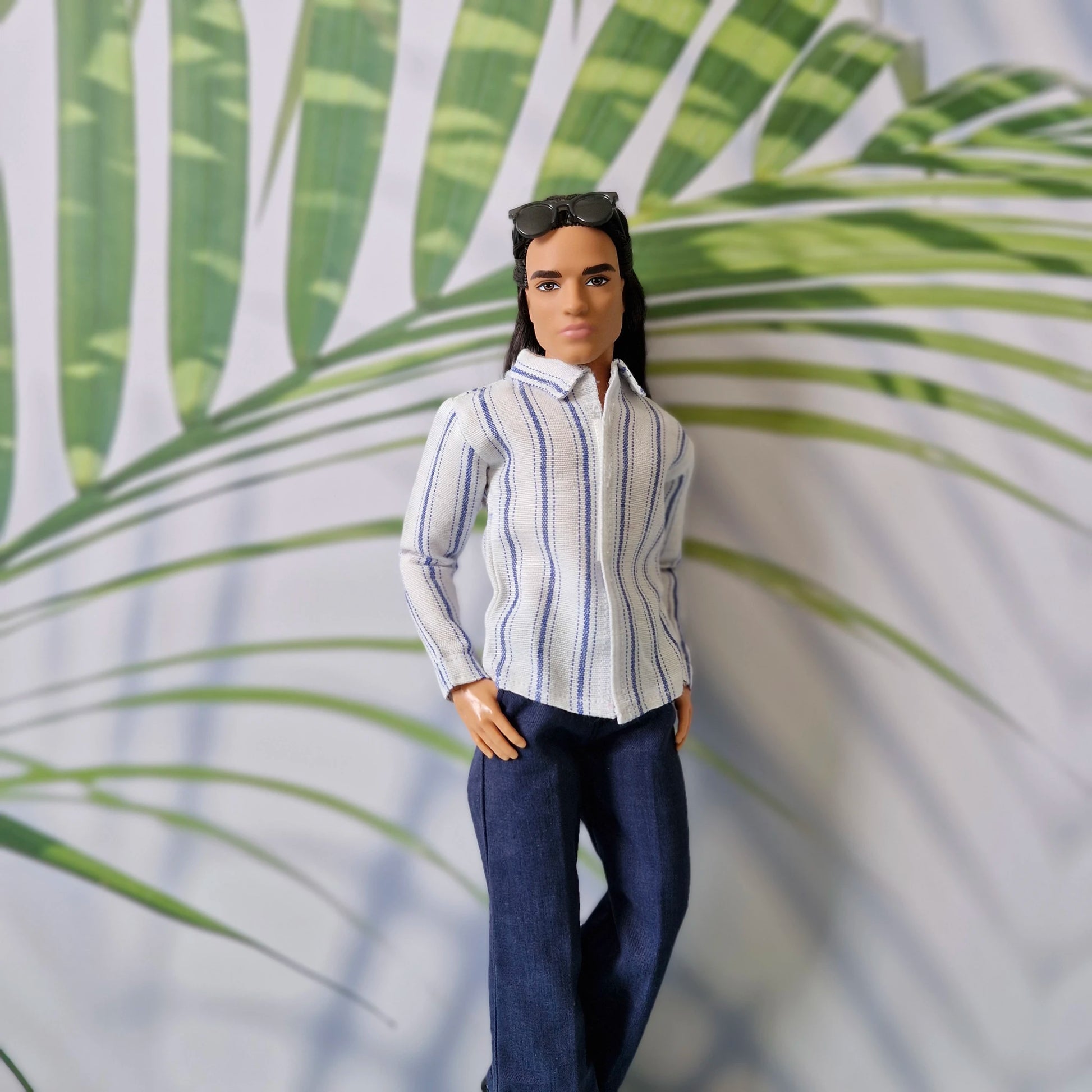Close-up of Ken doll wearing an untucked striped button-up shirt and navy blue trousers for a relaxed everyday style.