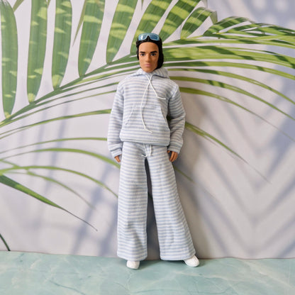 Full body shot of a Ken doll dressed in a trendy light blue striped hoodie and wide-leg trousers.