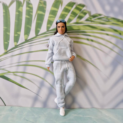 Ken doll posing with one leg crossed in a stylish blue striped hoodie and tapered sweatpants outfit.