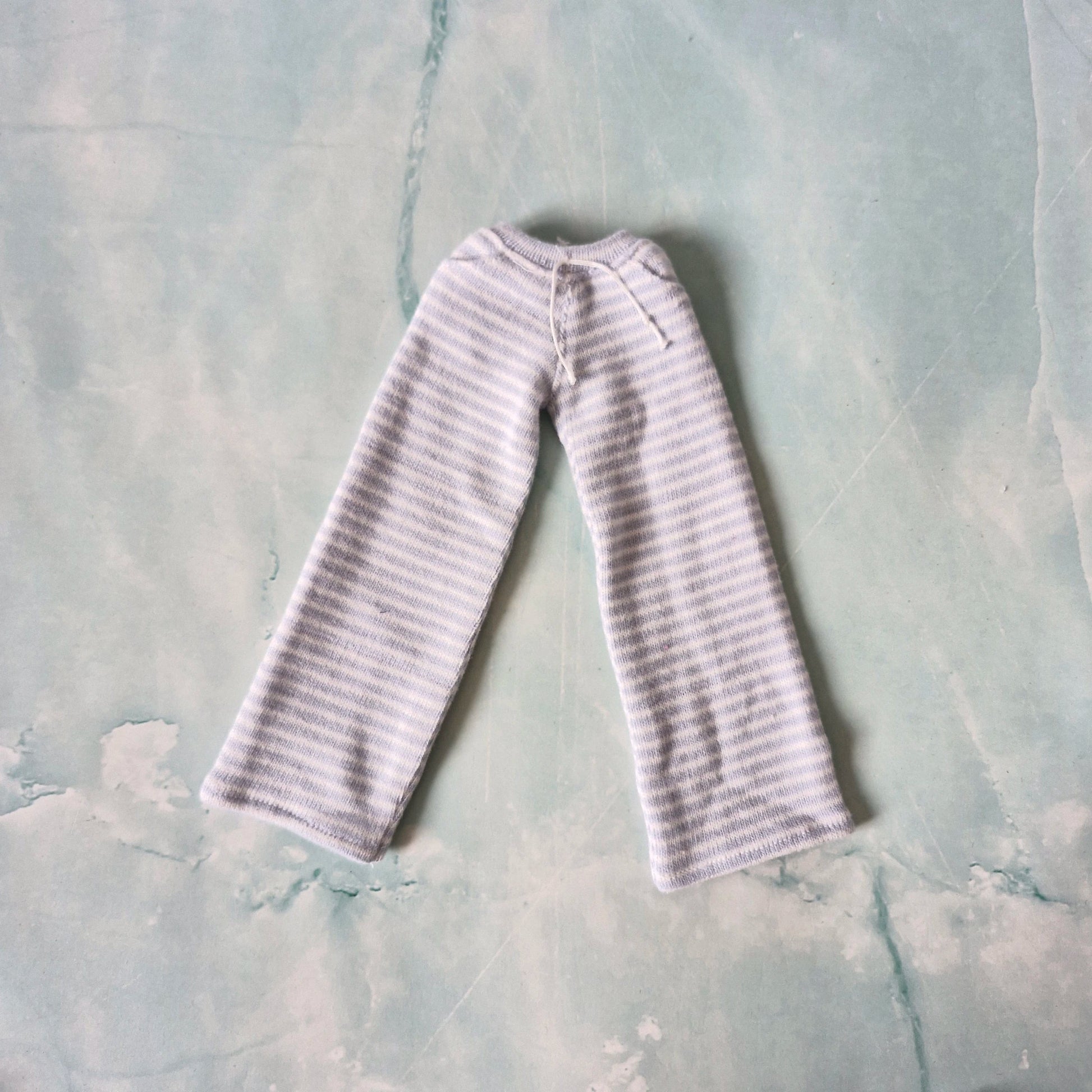 Flat lay of miniature doll clothes featuring wide-leg light blue and white striped pants.