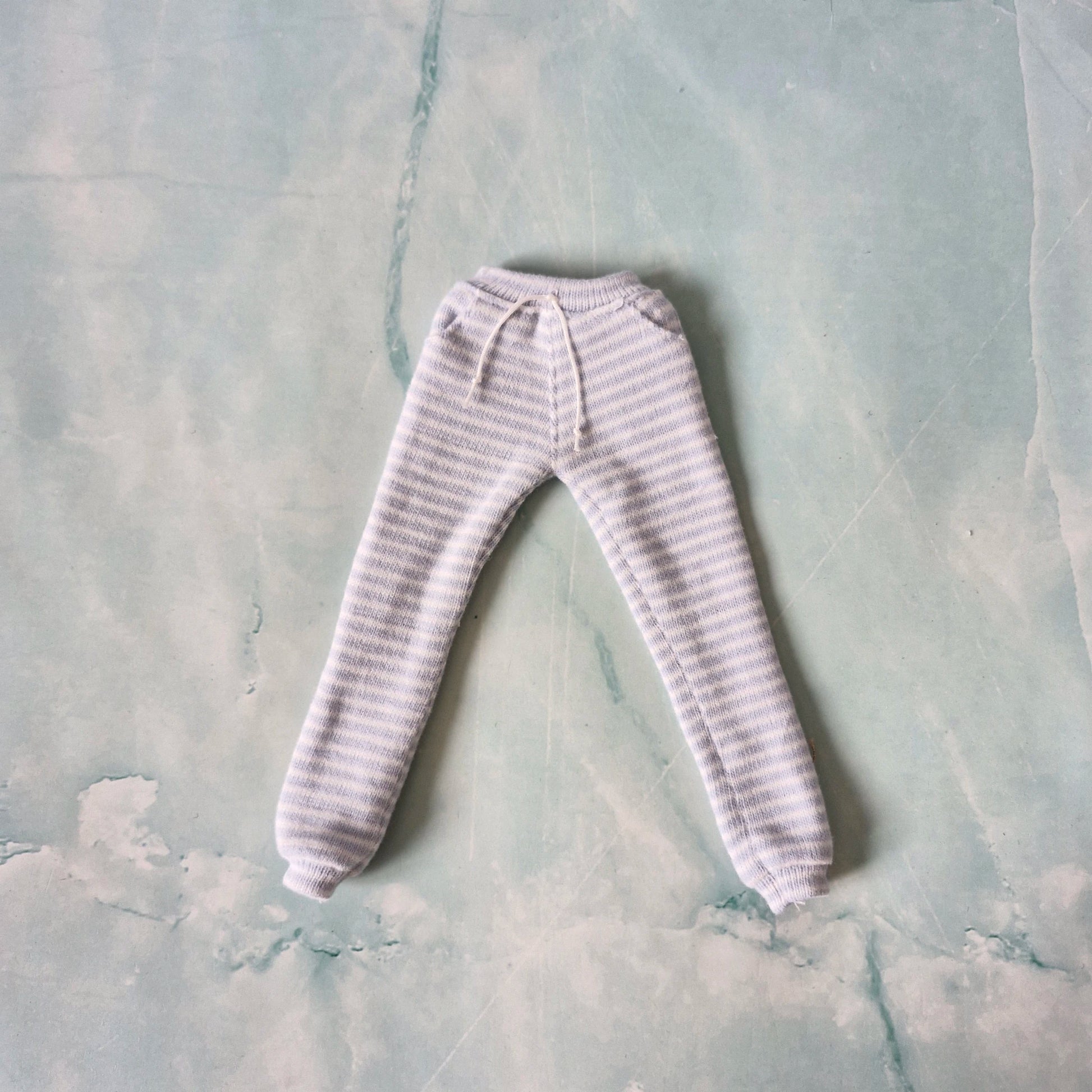 Flat lay of tapered doll sweatpants in a light blue and white striped pattern with a drawstring waist.