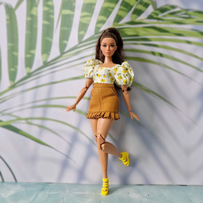 Full body shot of a Barbie doll modeling a yellow floral puff-sleeve top, brown ruffled skirt, and yellow strappy heels.