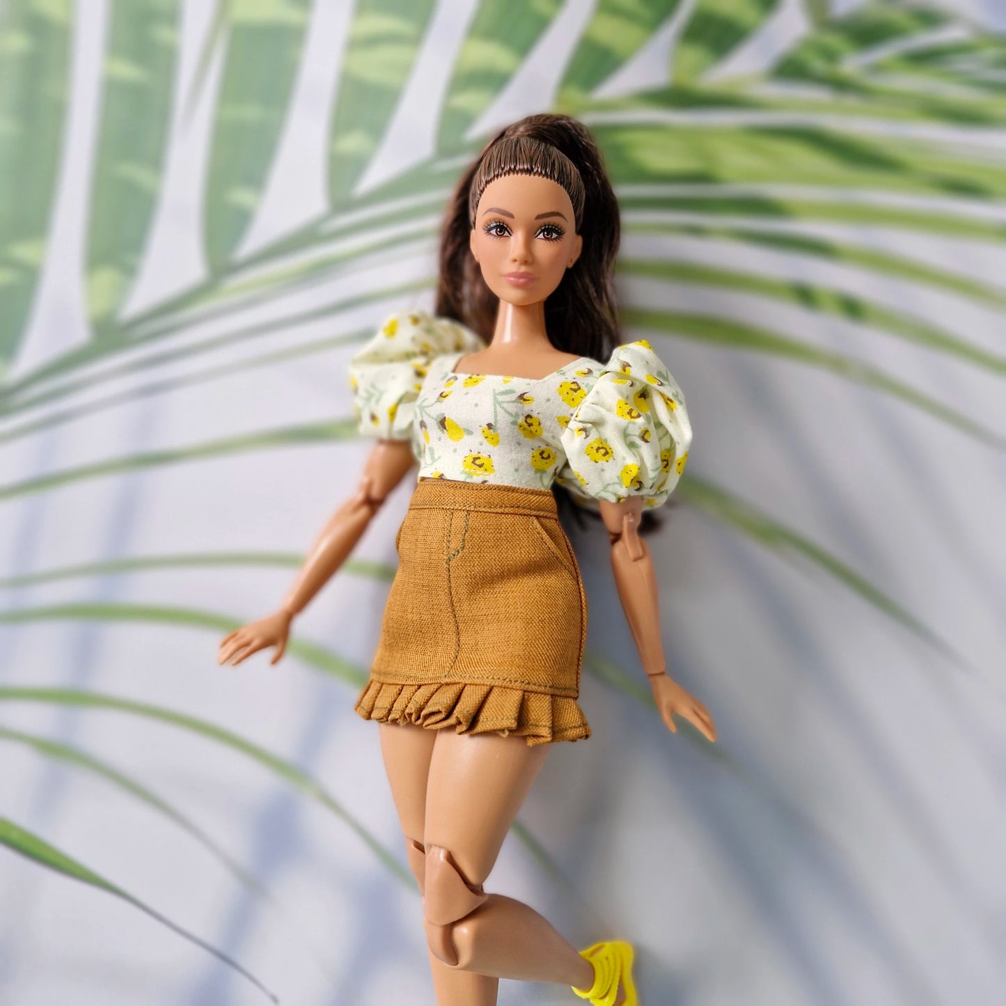 Close-up of Barbie doll wearing a vibrant yellow floral crop top with puff sleeves and a stylish brown ruffled skirt.