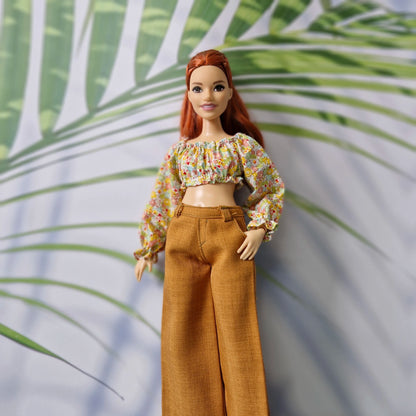 Close-up of Barbie doll dressed in a stylish floral off-shoulder top and high-waisted brown wide-leg pants.