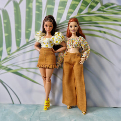 Two Barbie dolls showcasing summer fashion: one in a floral puff-sleeve top and brown ruffled skirt, the other in an off-shoulder top and wide-leg pants.