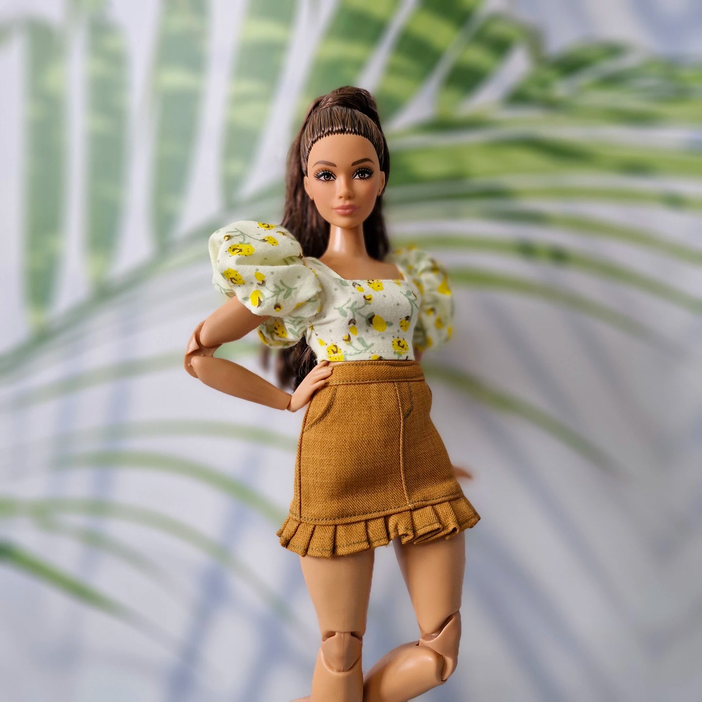Brunette Barbie doll posing in a cute floral puff-sleeve crop top and brown mini skirt with ruffle details.