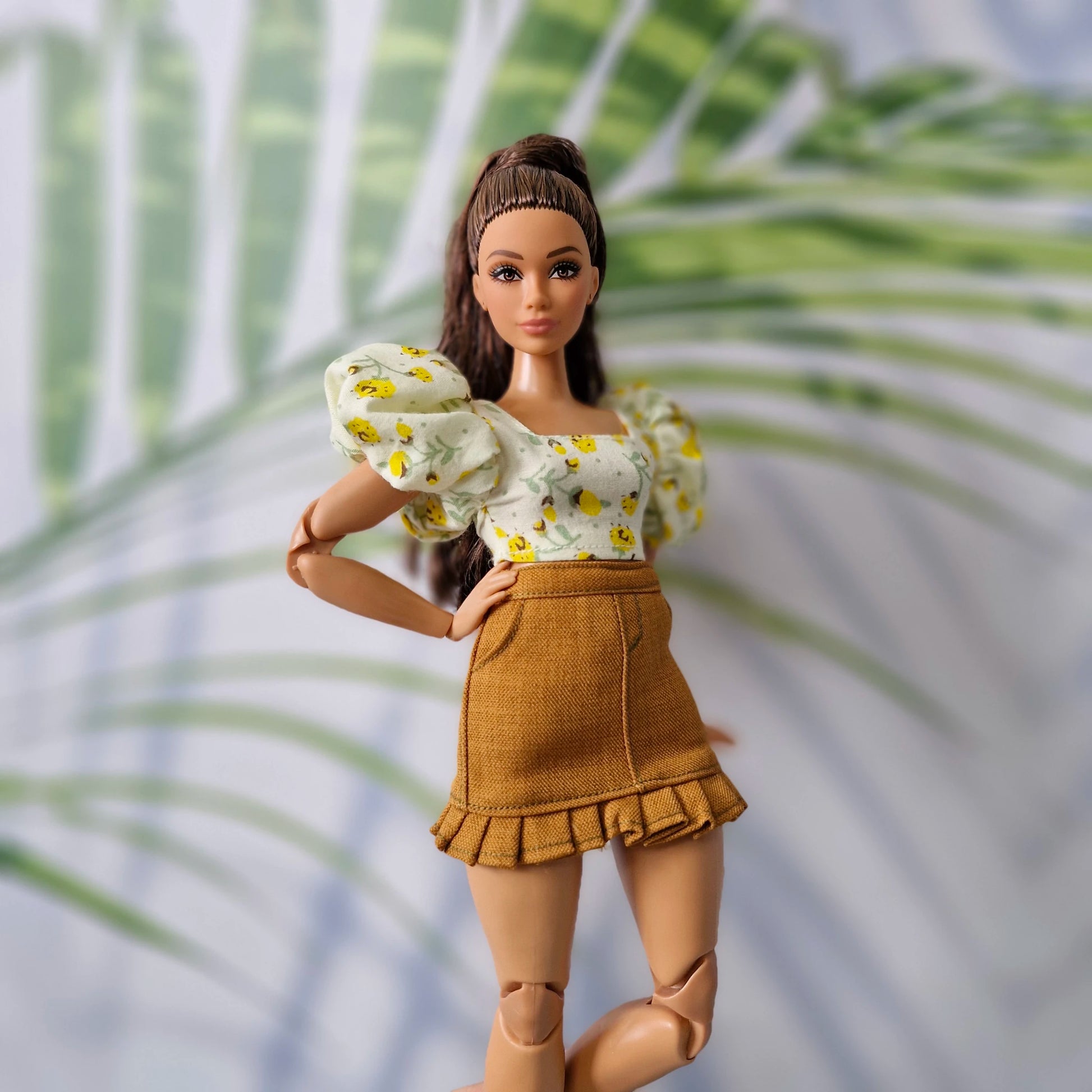 Brunette Barbie doll posing in a cute floral puff-sleeve crop top and brown mini skirt with ruffle details.