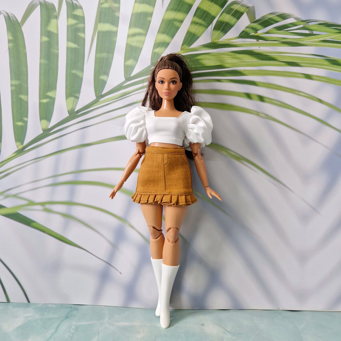 Barbie doll outfit featuring a white puff-sleeve crop top, brown ruffled mini skirt, and white knee-high boots.