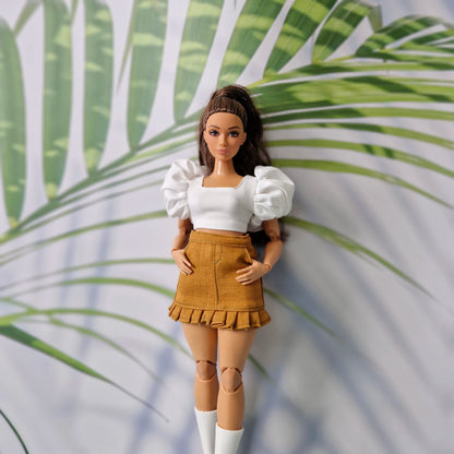 Top-down view of a brunette Barbie doll wearing a stylish white puff-sleeve top and brown mini skirt.