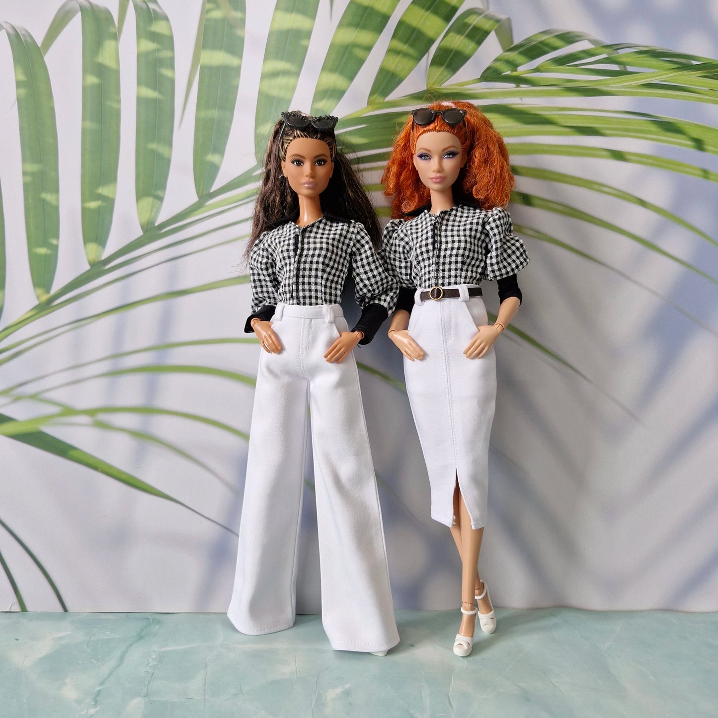Two fashion dolls showcasing clothes for Barbie: one in white wide-leg pants and the other in a white pencil skirt, both wearing matching gingham tops.